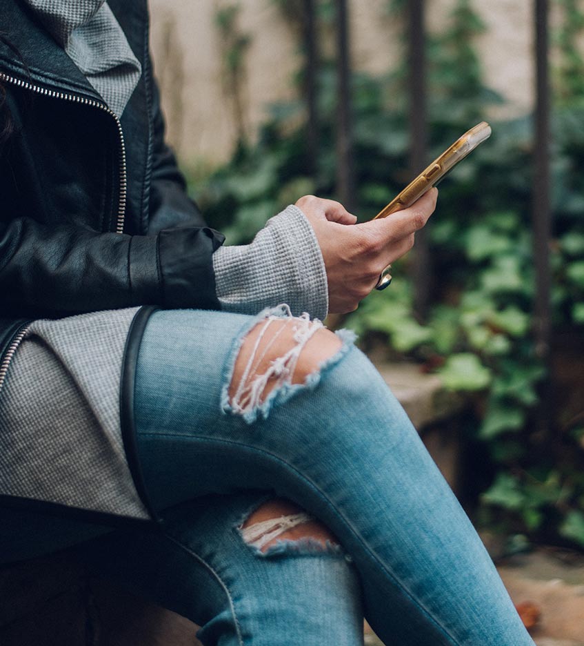 kvinna sittandes i trasiga jeans med mobil i hand