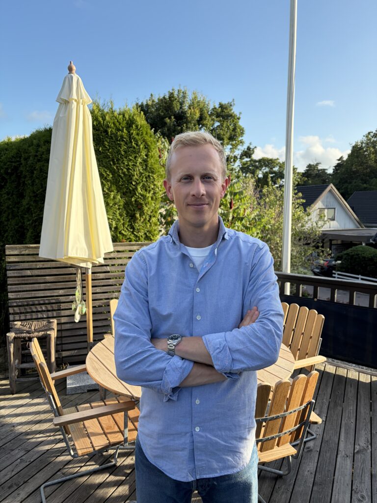 Blond man på altan med parasoll i bakgrund